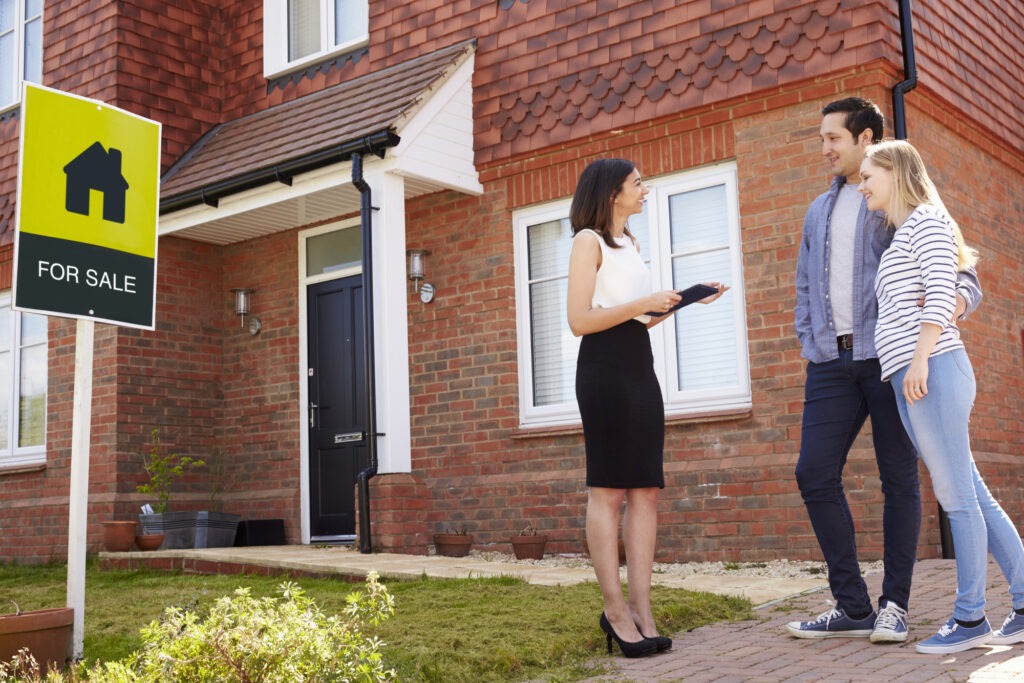 Realtor Outside House For Sale With Young Couple.